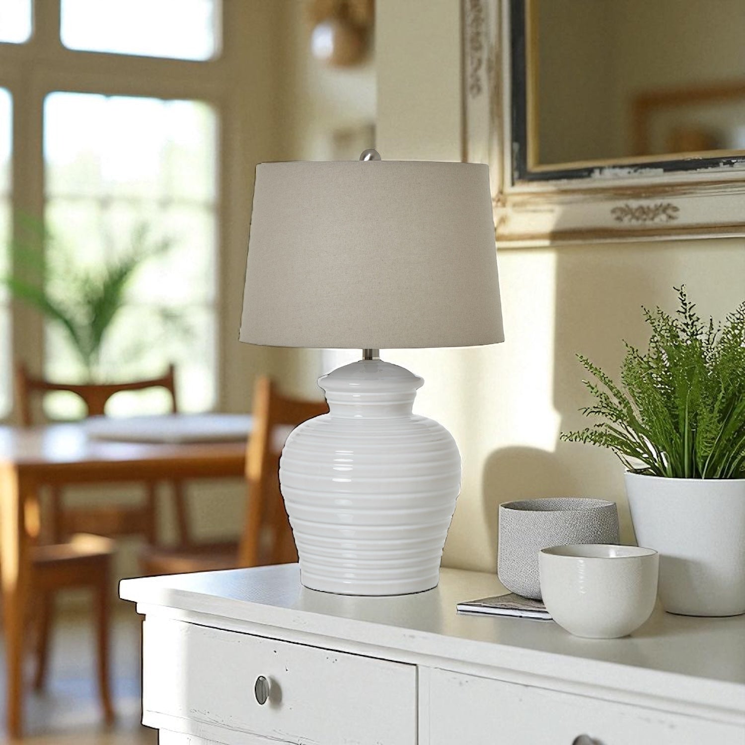 White ceramic lamp on a wooden side table with a plant and books in a room setting.