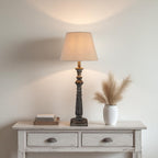 Table lamp on a wooden side table with decorative items against a plain wall.