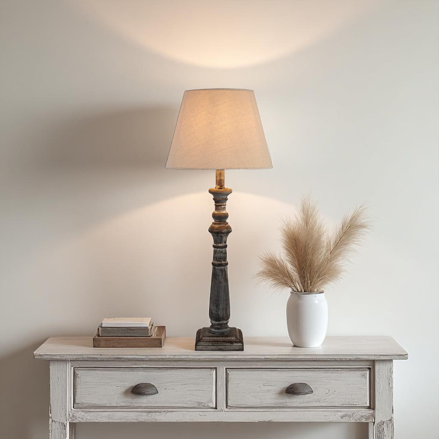 Table lamp on a wooden side table with decorative items against a plain wall.