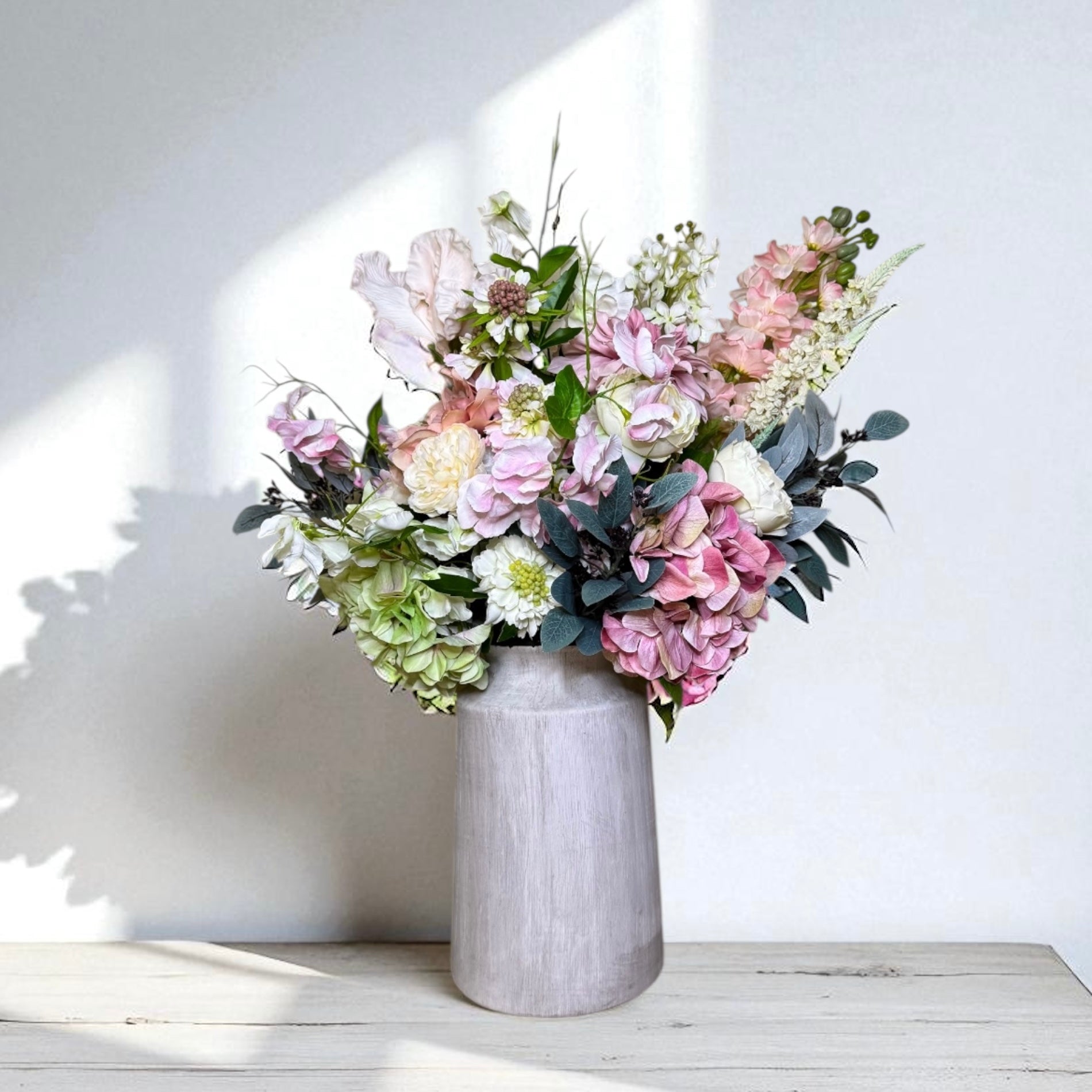 Bouquet of pink, white and green flowers in a grey vase on a white surface with a white wall background