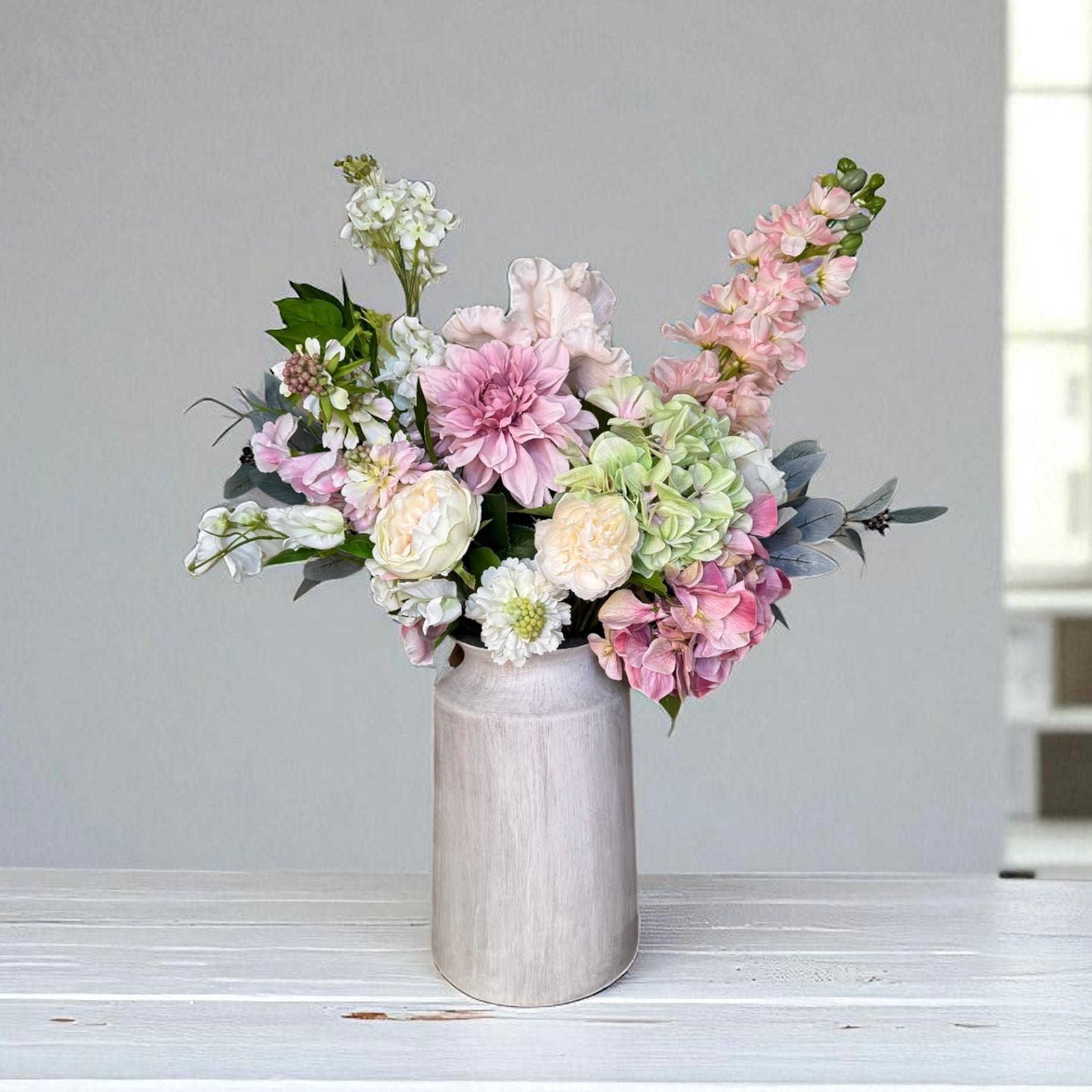 Bouquet of pink, white, and green flowers in a light grey vase on a light wooden surface with a neutral background.