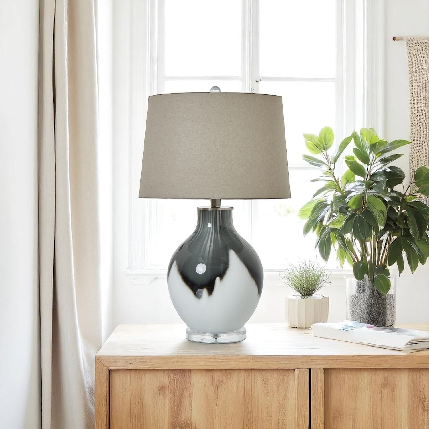 Table lamp with a beige shade on a wooden side table next to a plant