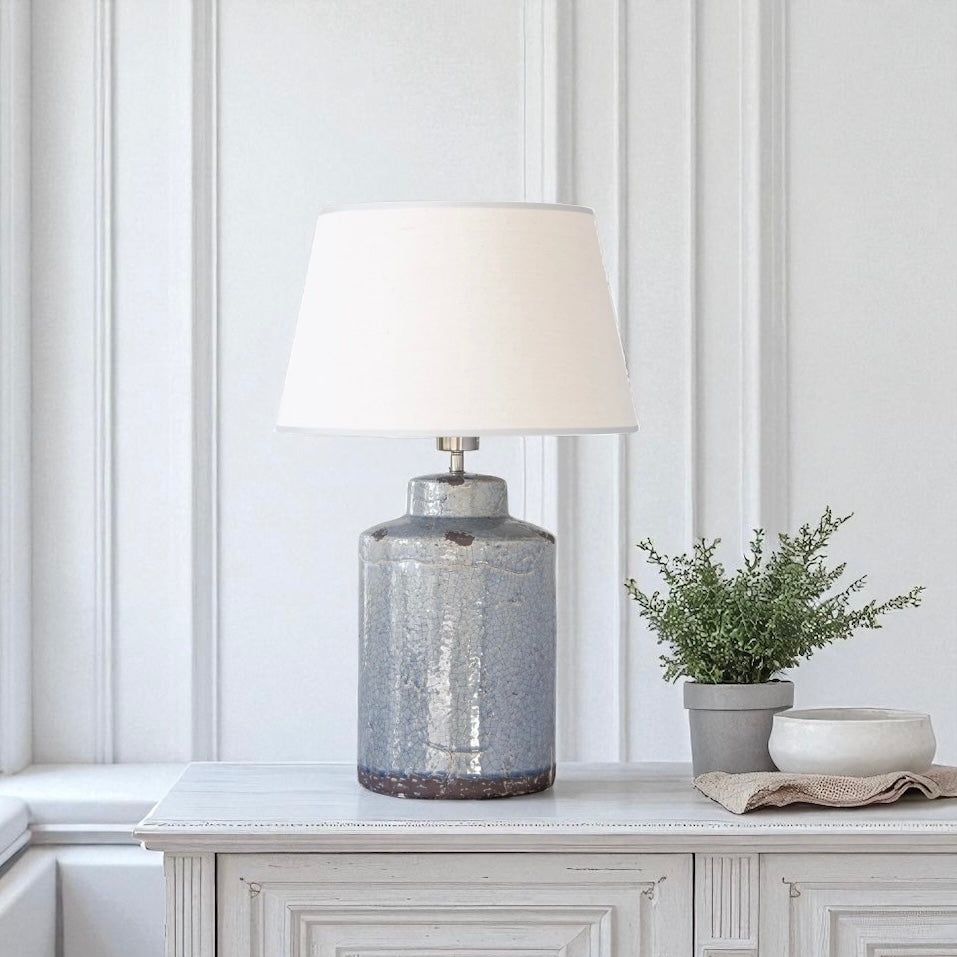 Decorative lamp with a textured blue base on a white surface against a white panelled wall.