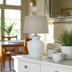 White ceramic lamp on a wooden side table with a plant and books in a room setting.
