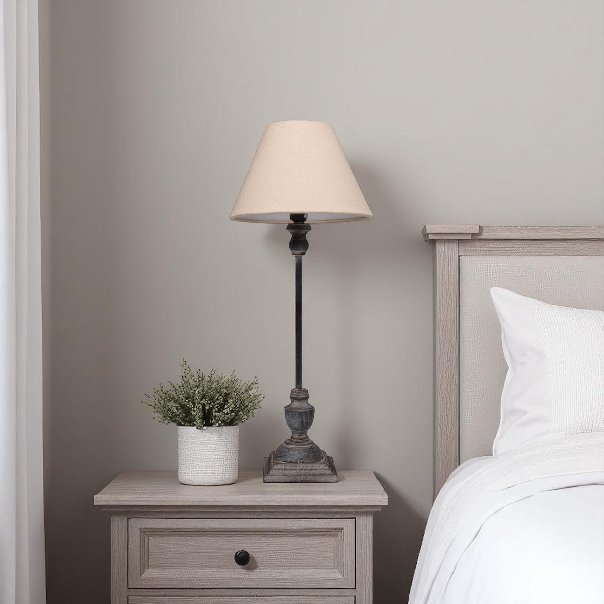 Bedside table with table lamp and plant next to a bed in a bedroom setting