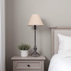 Bedside table with table lamp and plant next to a bed in a bedroom setting