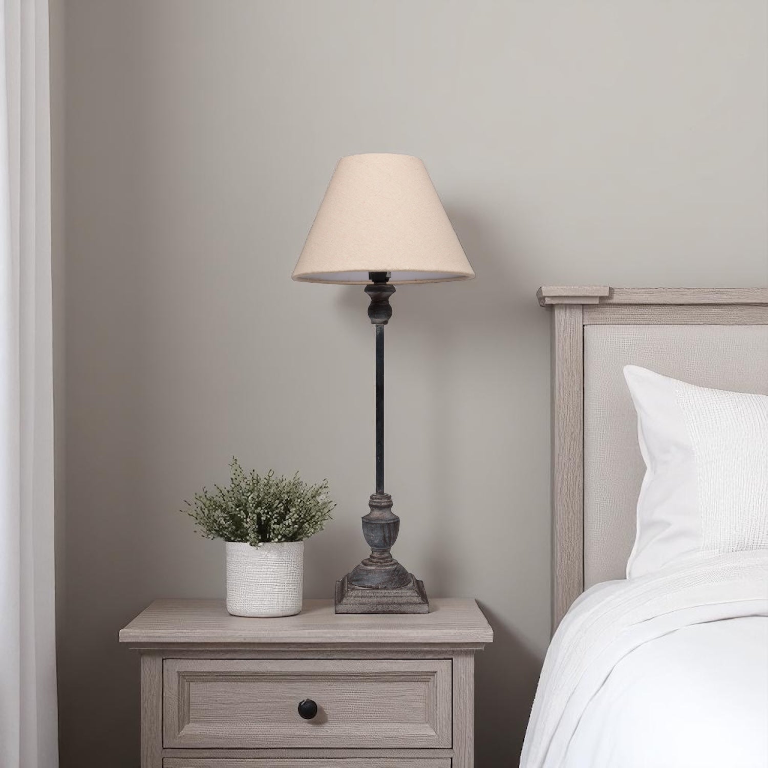 Bedside table with table lamp and plant next to a bed in a bedroom setting