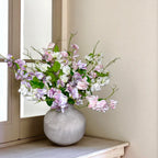 Bouquet of pink, purple and white flowers in a grey vase on a windowsill.
