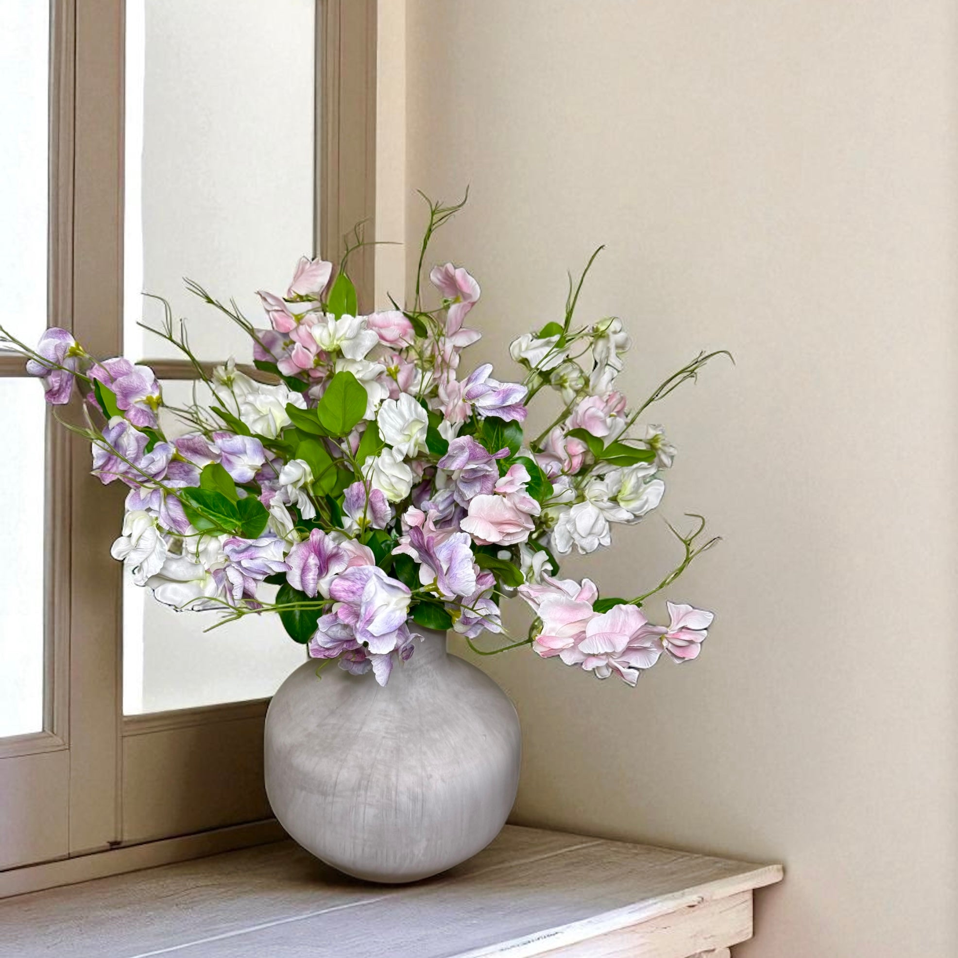 Bouquet of pink, purple and white flowers in a grey vase on a windowsill.