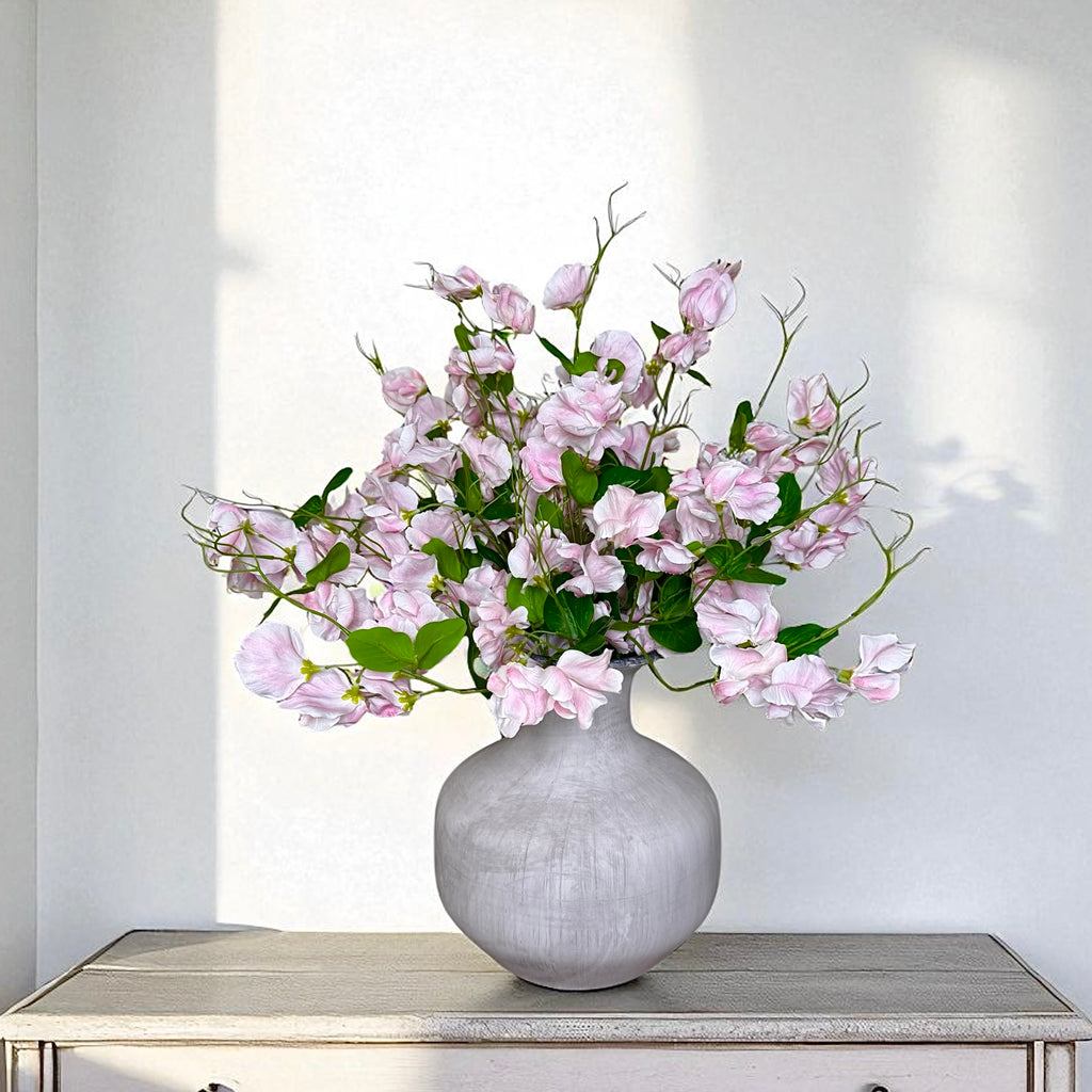 Bouquet of pink sweet pea flowers in a grey vase on a white surface