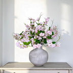 Bouquet of pink sweet pea flowers in a grey vase on a white surface