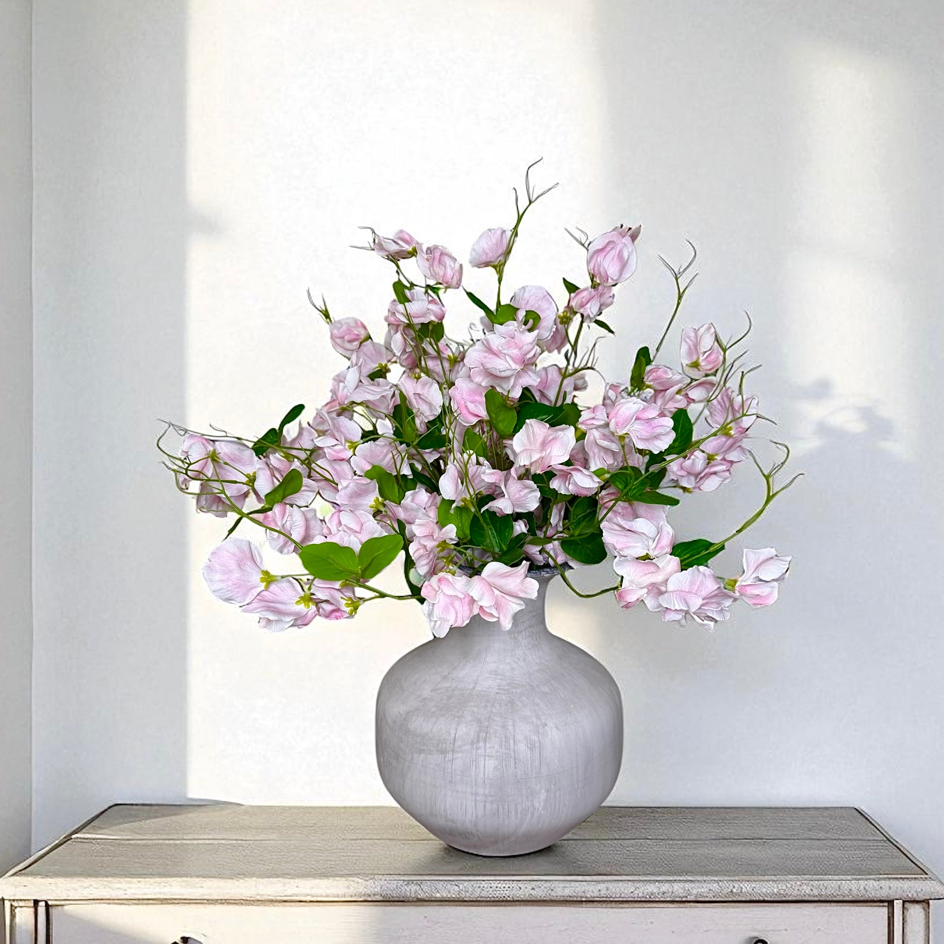 Bouquet of pink sweet pea flowers in a grey vase on a white surface