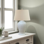 White woven textured table lamp on a wooden side table with a window in the background