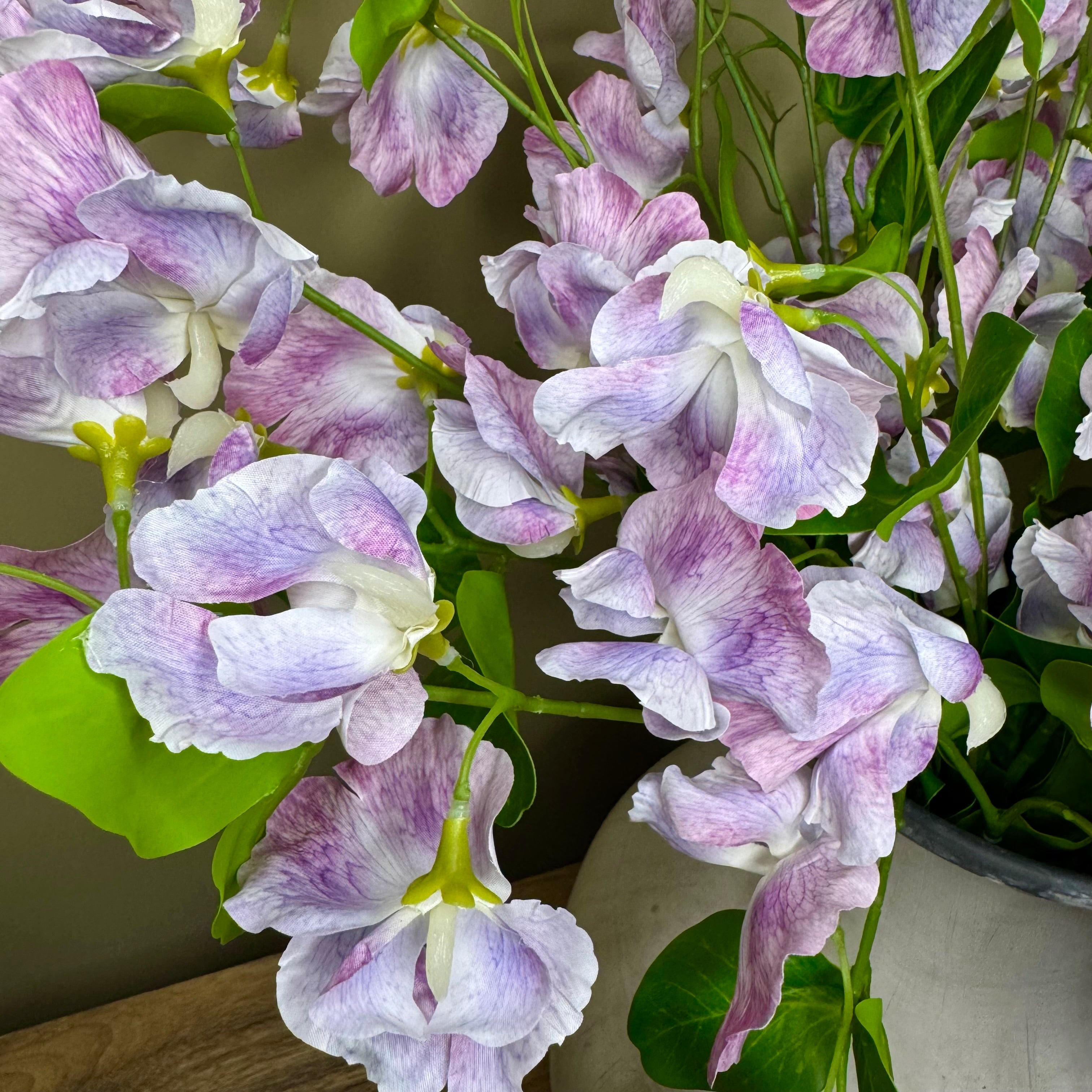 Close-up of purple sweet pea flowers with green leaves on a neutral background