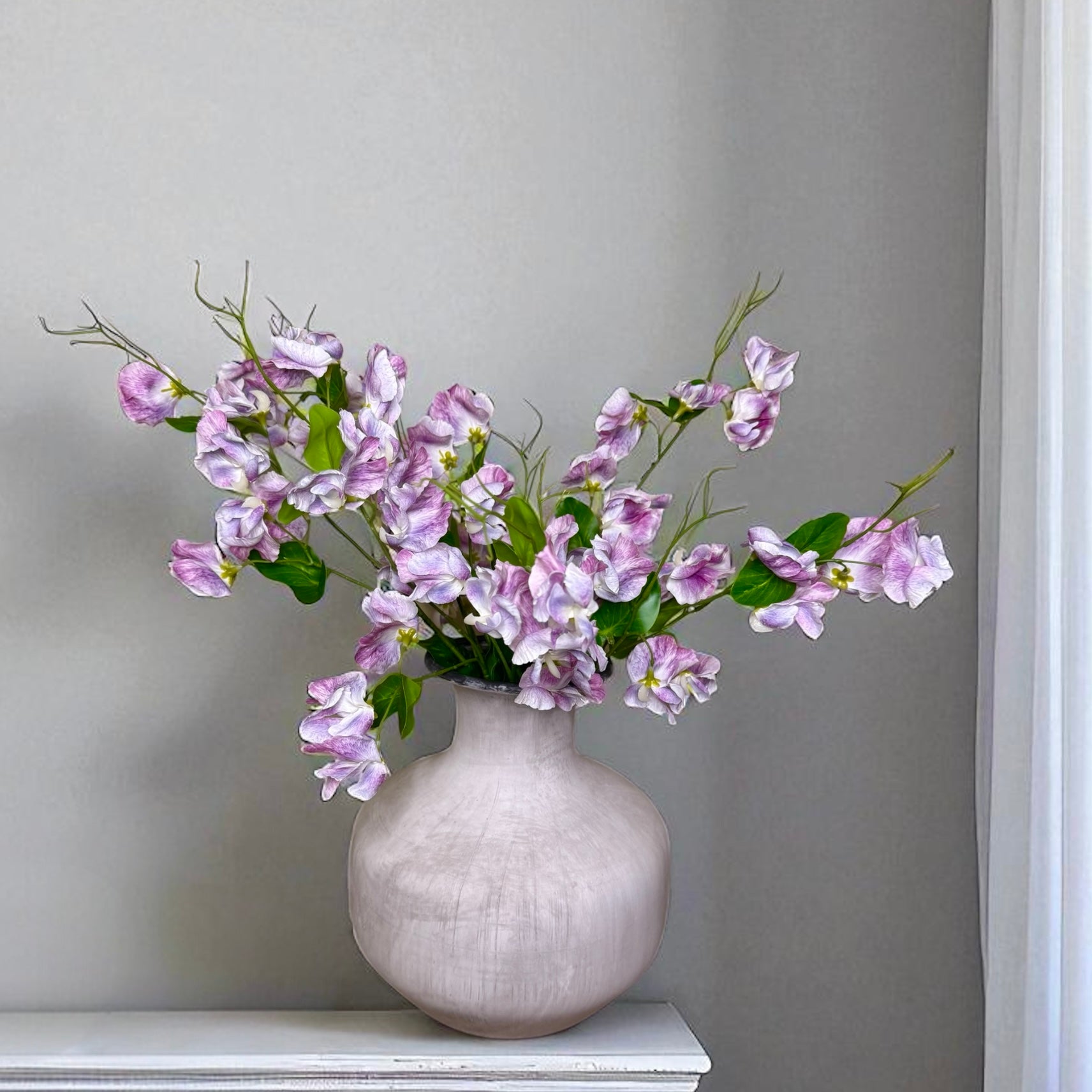 Light grey vase with purple sweet pea flowers on a grey background