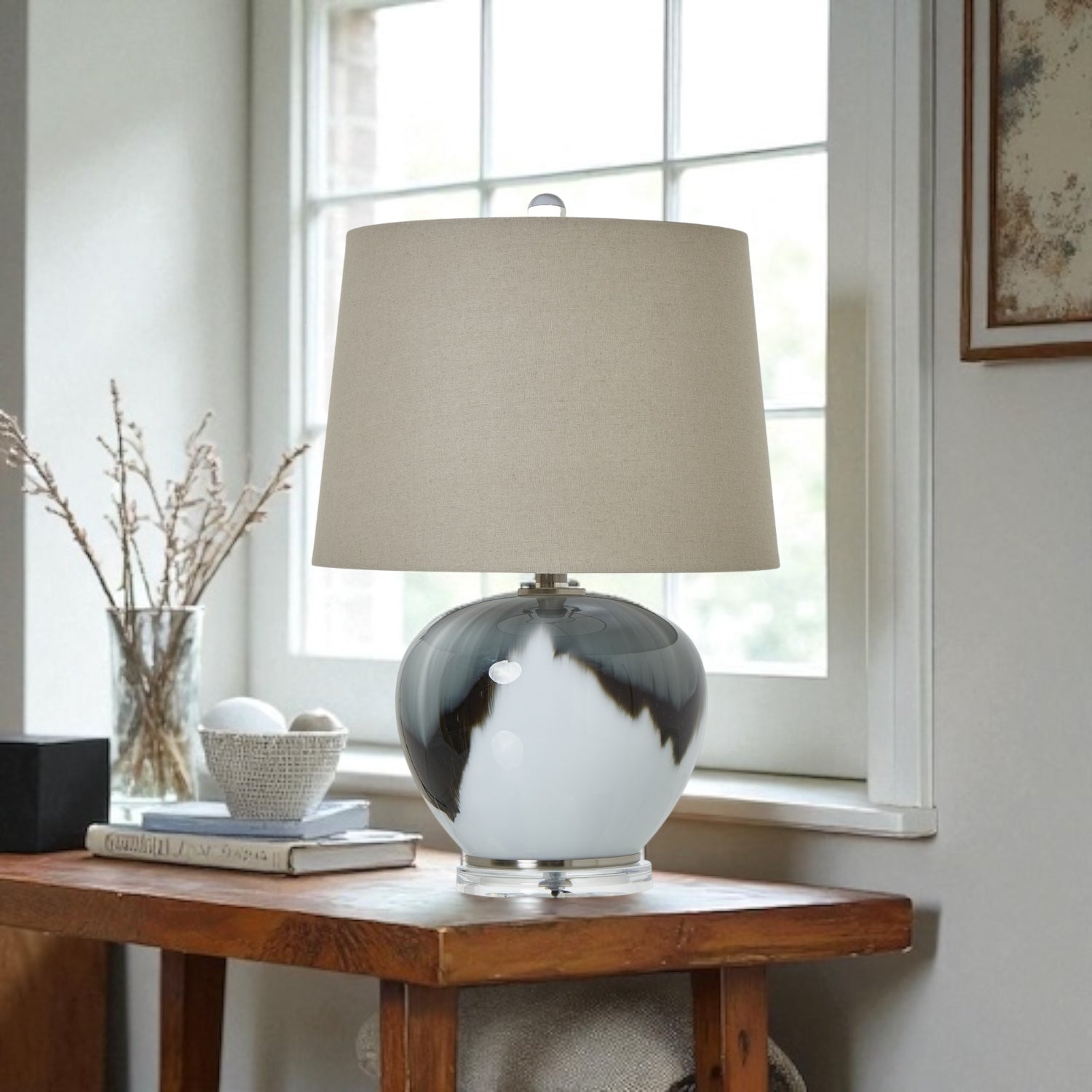 Decorative lamp with a beige shade on a wooden table near a window.