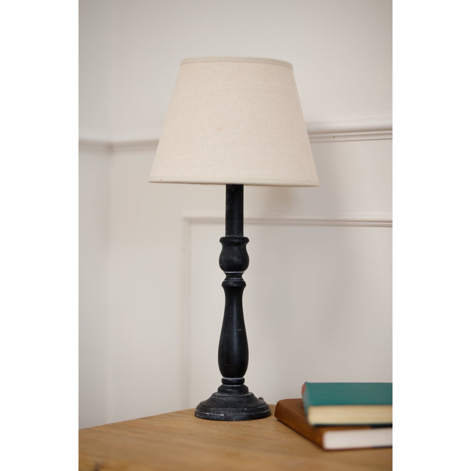 Verona Table lamp with a beige shade on a wooden surface next to books against a white wall.