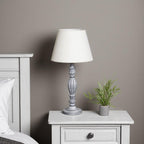 Grey wooden bedside table with a white lamp and small plant against a grey wall.