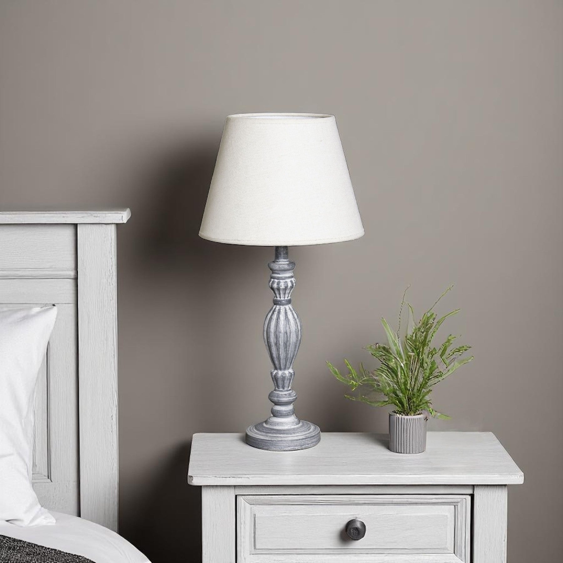 Grey wooden bedside table with a white lamp and small plant against a grey wall.