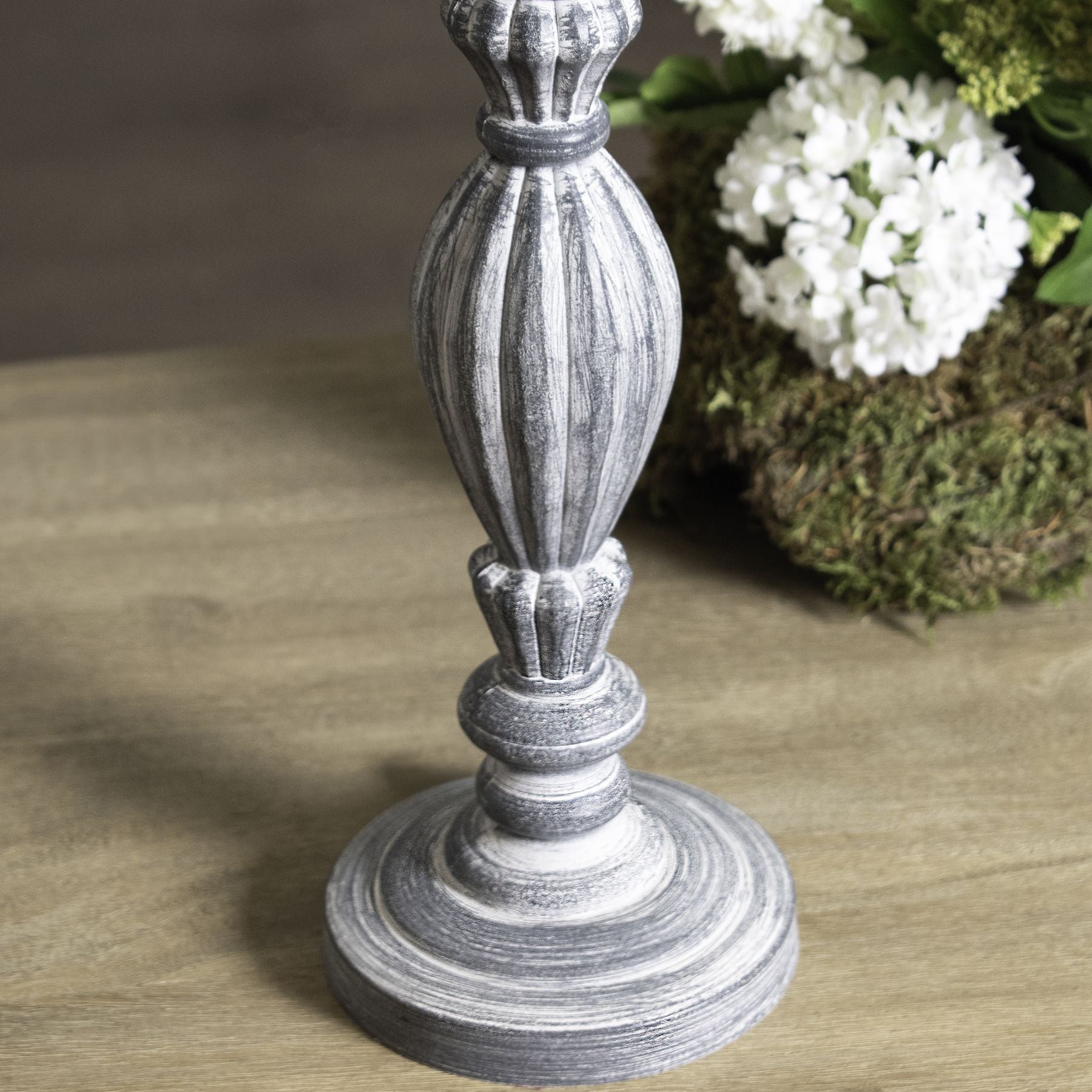 Carved grey wooden table lamp on a wooden surface with flowers in the background