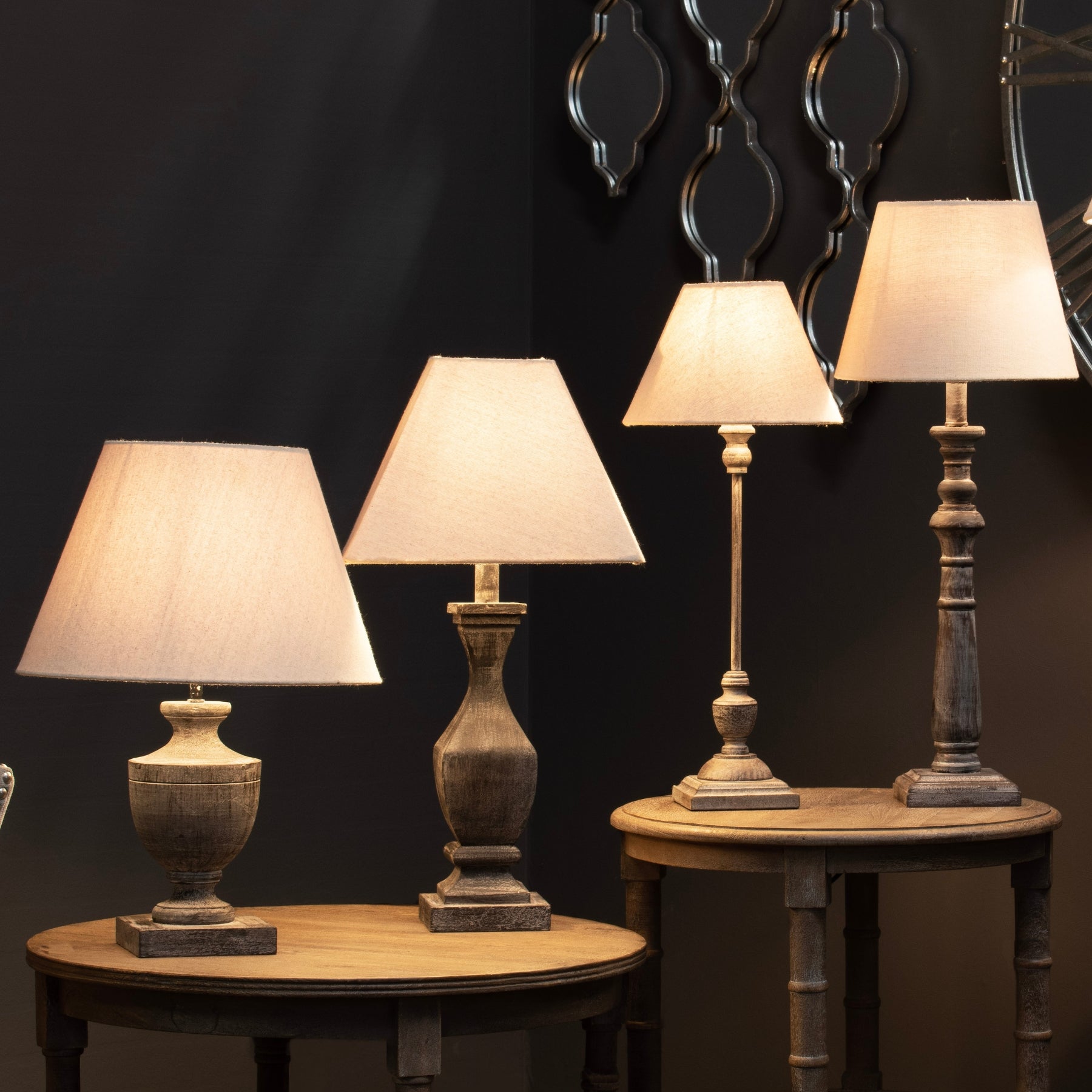 Set of four table lamps on wooden tables against a dark wall with decorative mirrors.