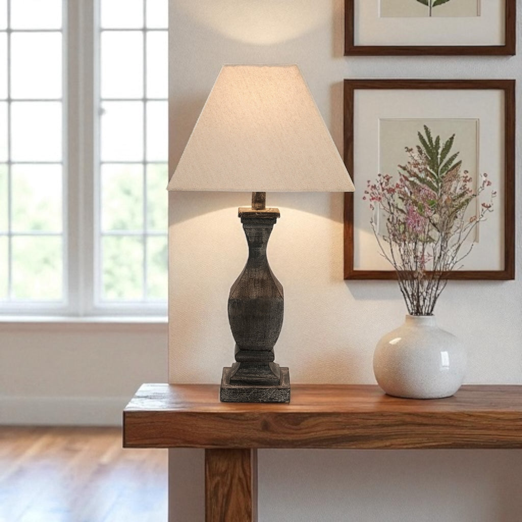 Table lamp on a wooden console table with a vase and framed picture in a room.