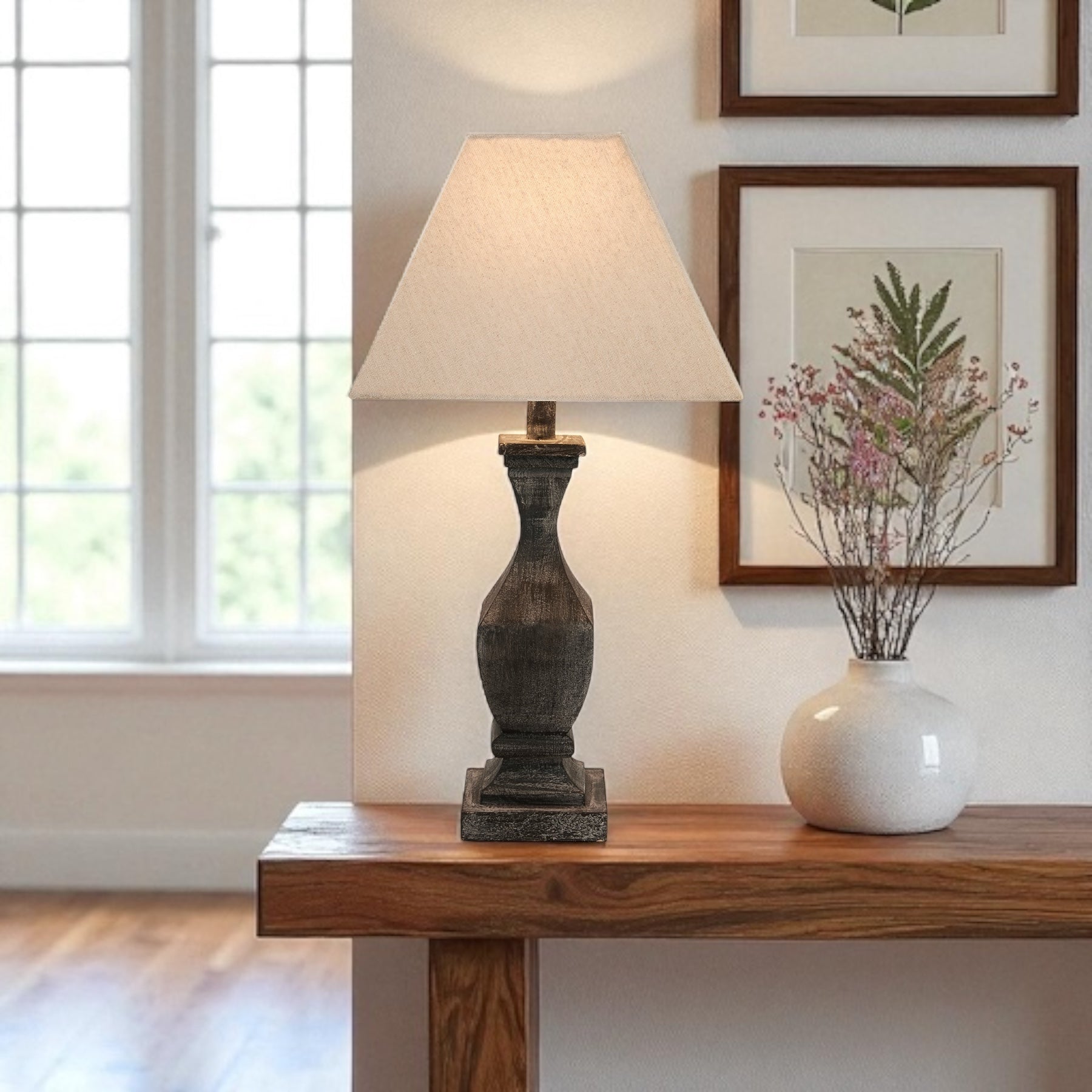 Table lamp on a wooden console table with a vase and framed picture in a room.