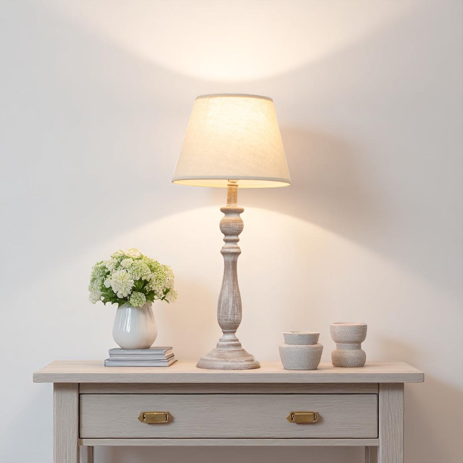 Table lamp on a wooden table with decorative items against a white wall