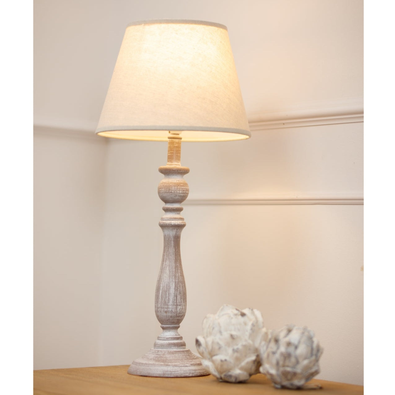 Table lamp with a wooden base and cream shade on a wooden surface.