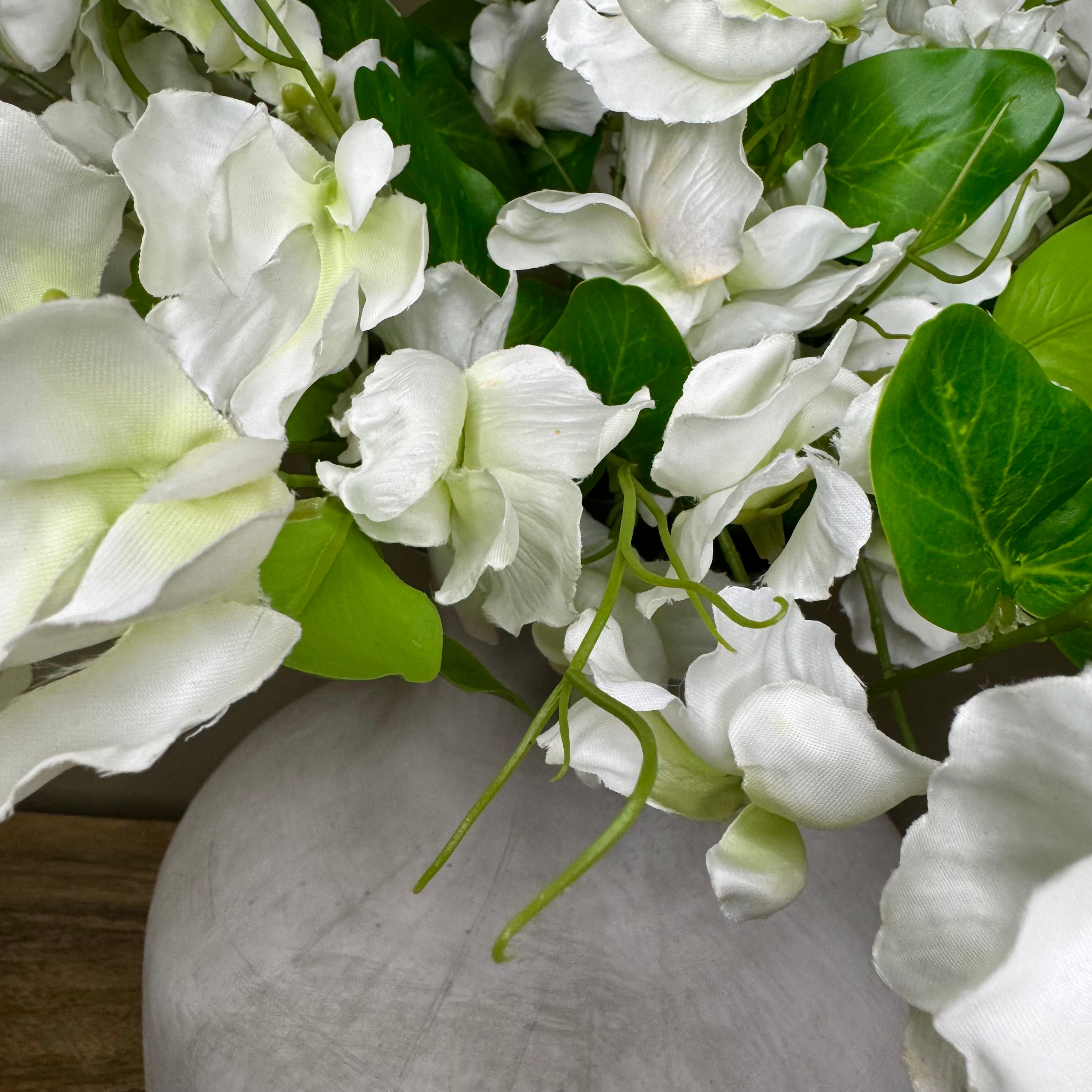 Bouquet of white sweet pea flowers with green leaves in a grey vase.