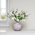Grey vase with white sweet pea flowers on a white surface