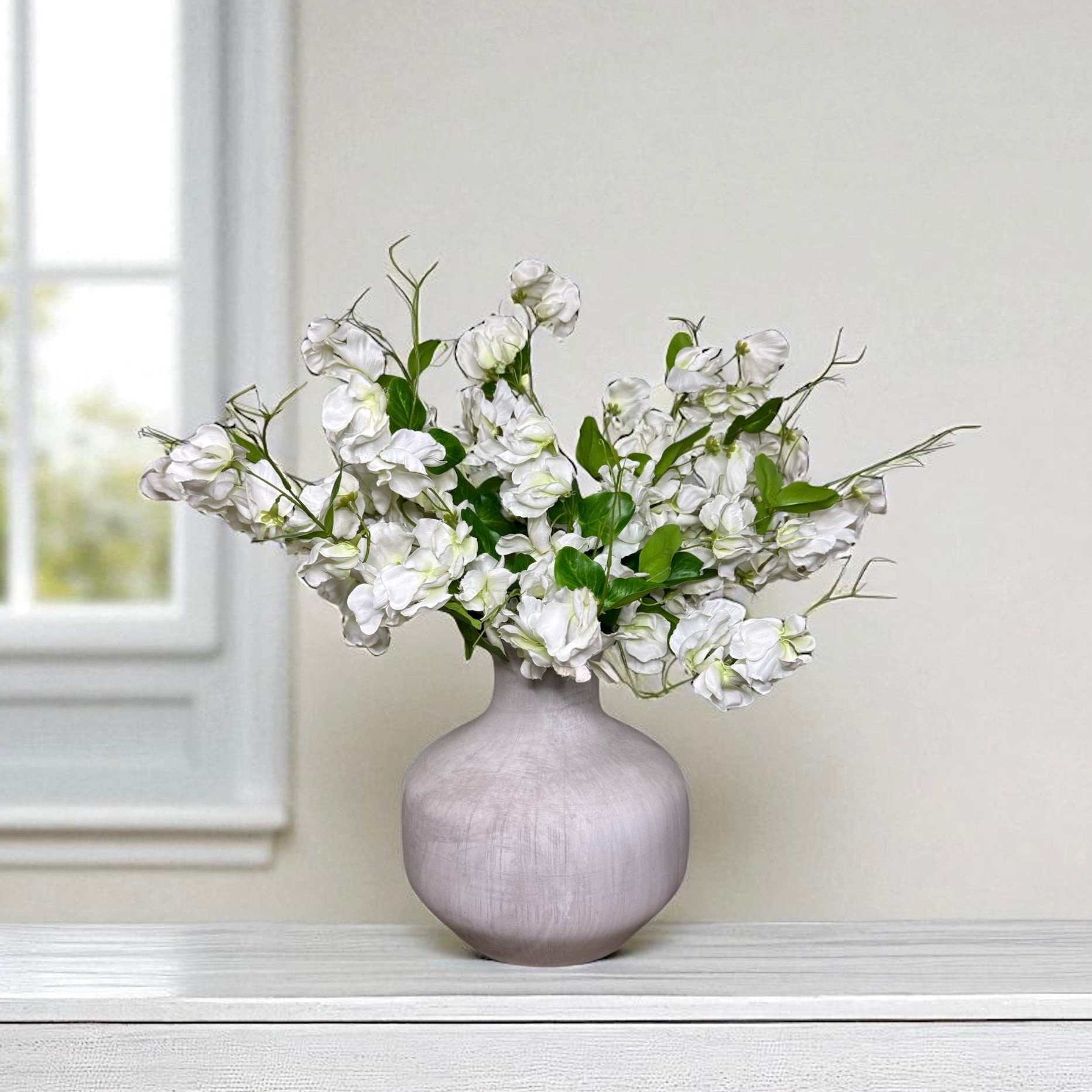 Grey vase with white sweet pea flowers on a white surface