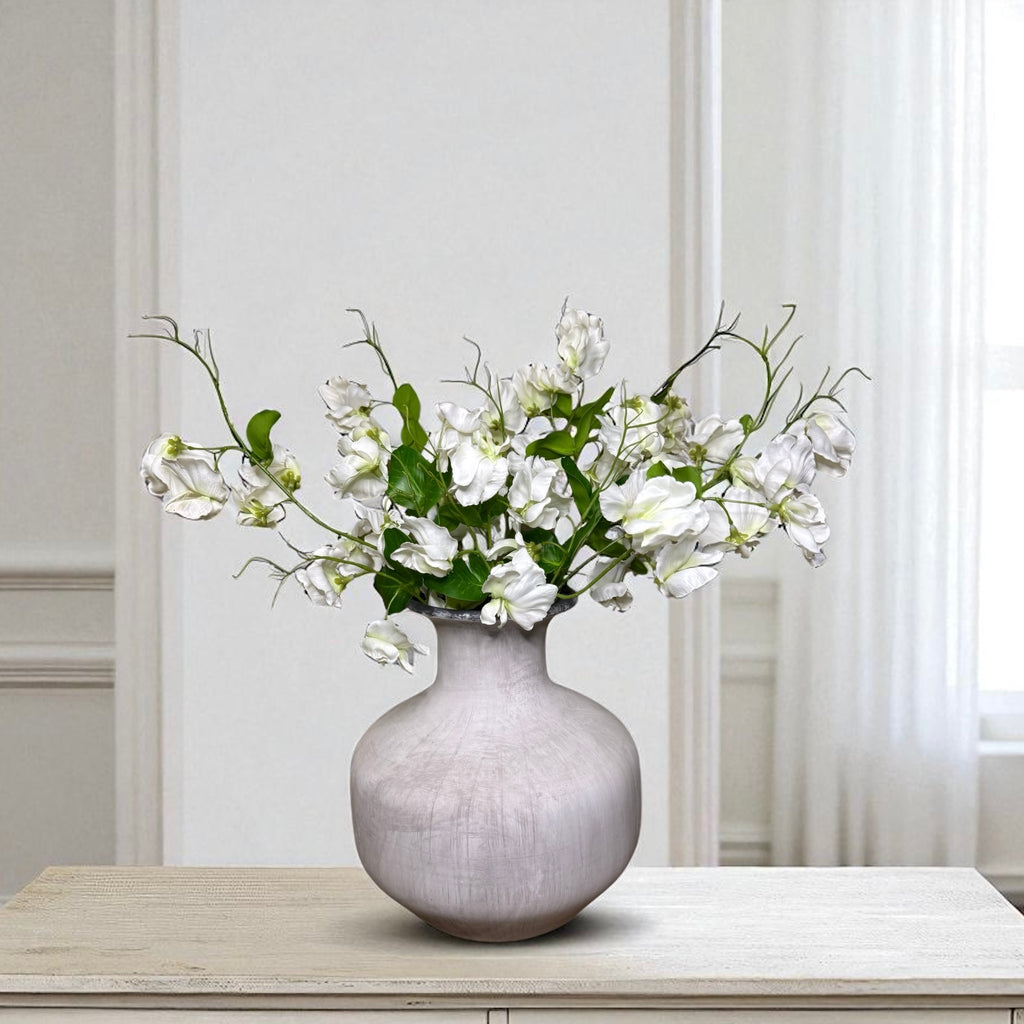 Grey vase with white sweet pea flowers on a wooden table against a light grey wall.