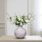 Grey vase with white sweet pea flowers on a wooden table against a light grey wall.