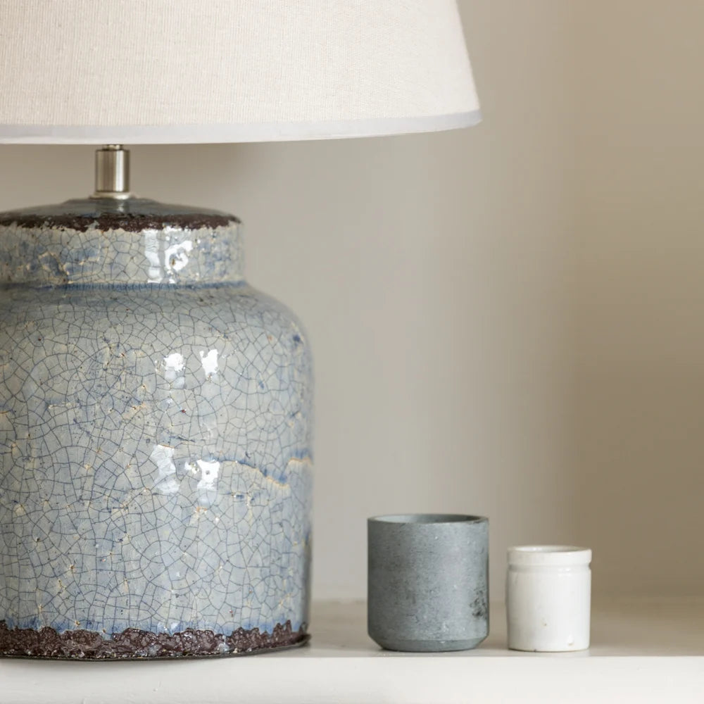 Blue ceramic table lamp with textured surface next to two smaller ceramic containers on a neutral background