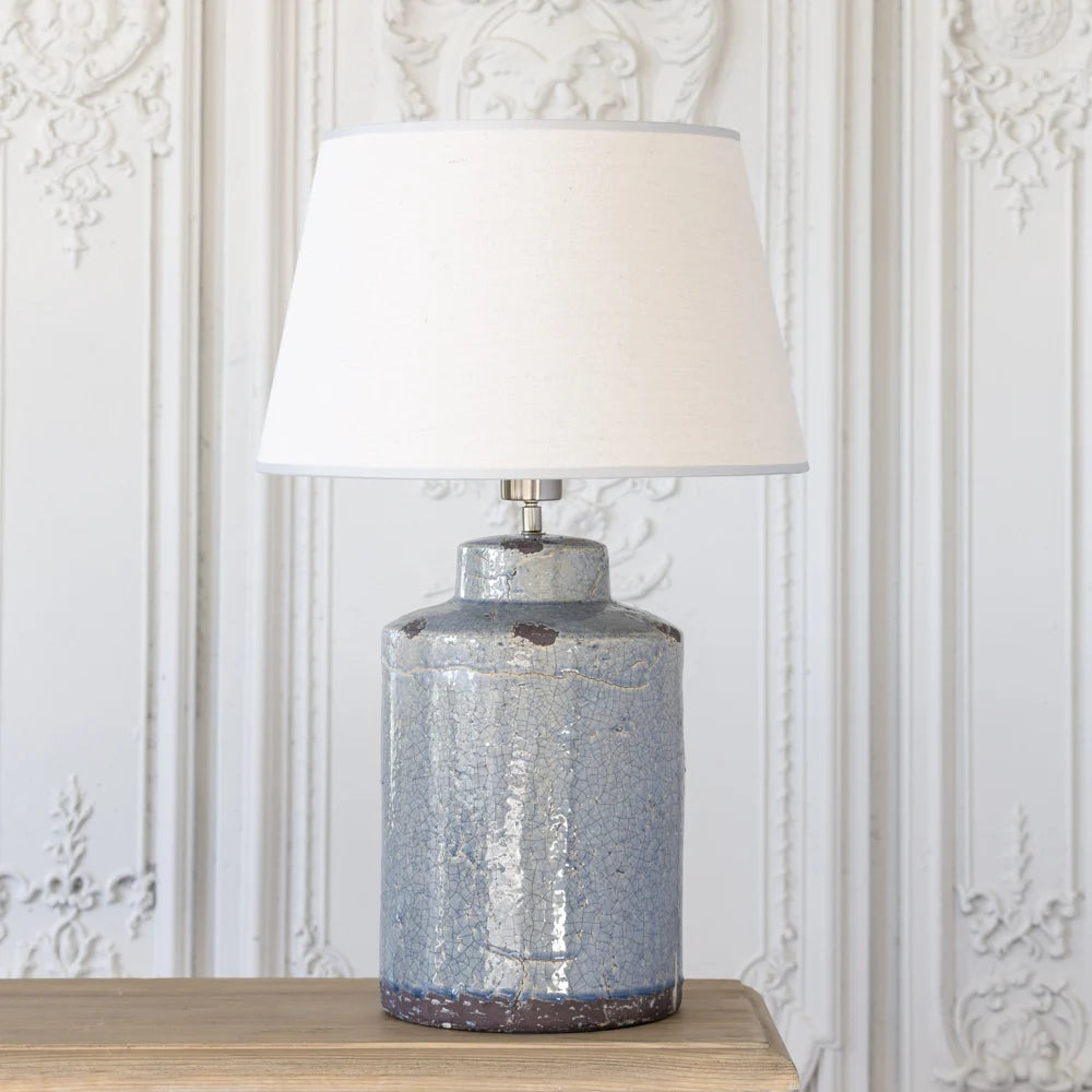 Table lamp with a textured blue base and cream shade on a wooden surface.