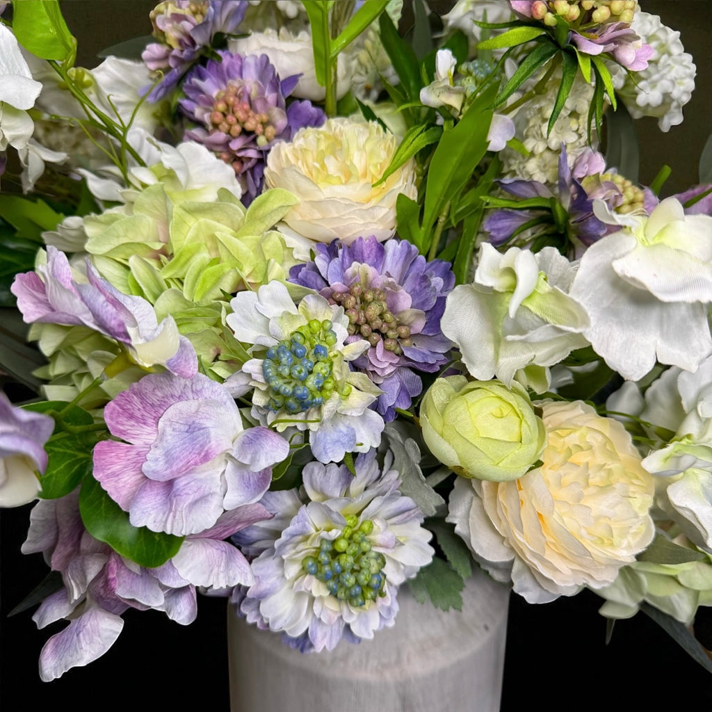 Bouquet of purple and white flowers with a white vase on a dark background