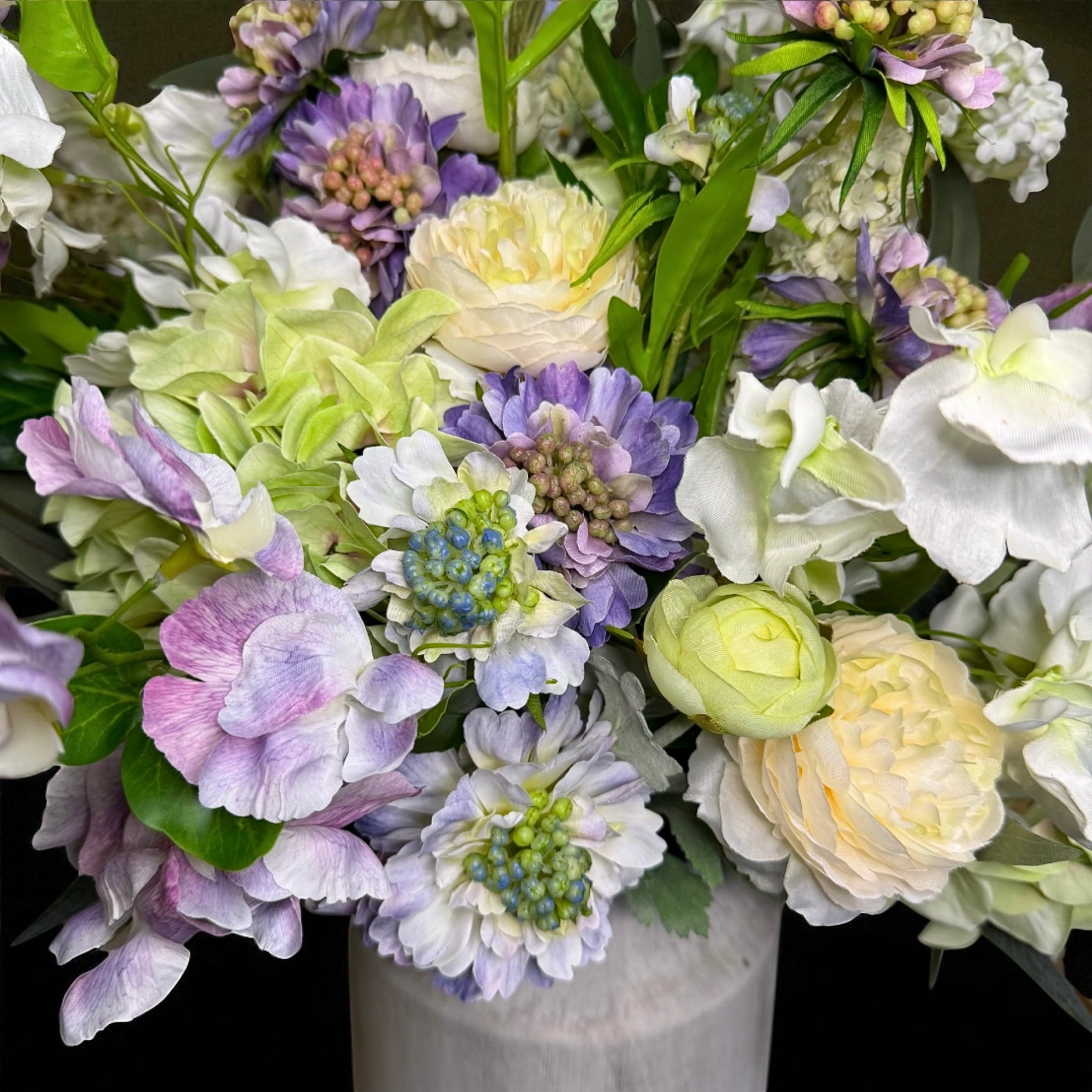 Bouquet of purple and white flowers with a white vase on a dark background